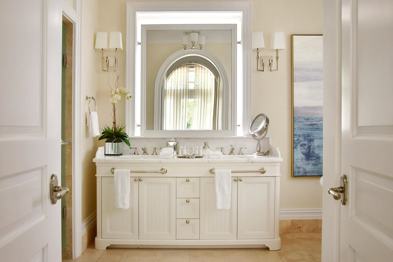 A bathroom vanity with orchids and a lit mirror