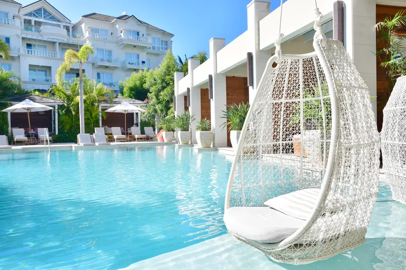 A resort pool with hanging chairs at the water's edge