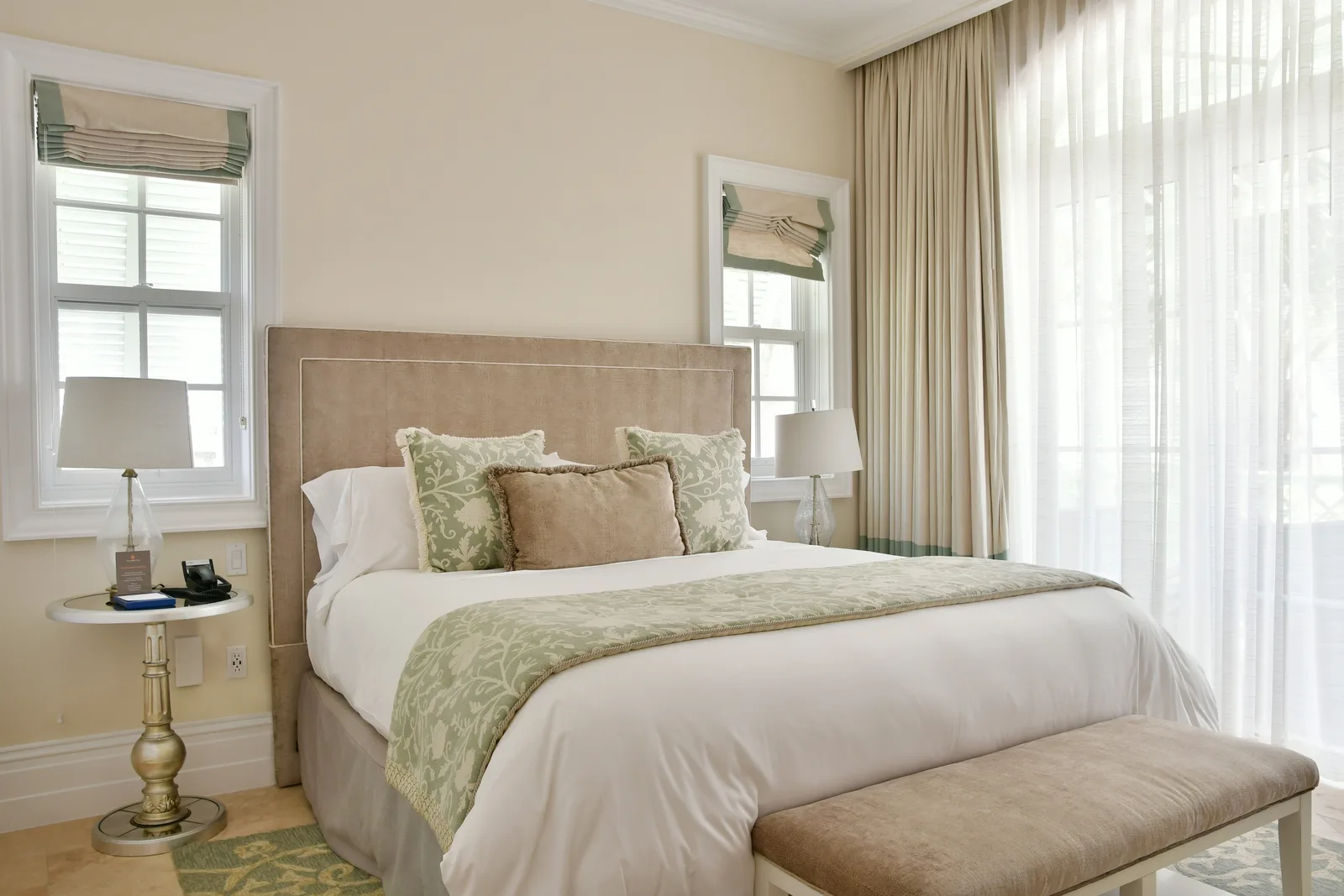 A guest bedroom in beige and sage, with a bench at the foot of the bed