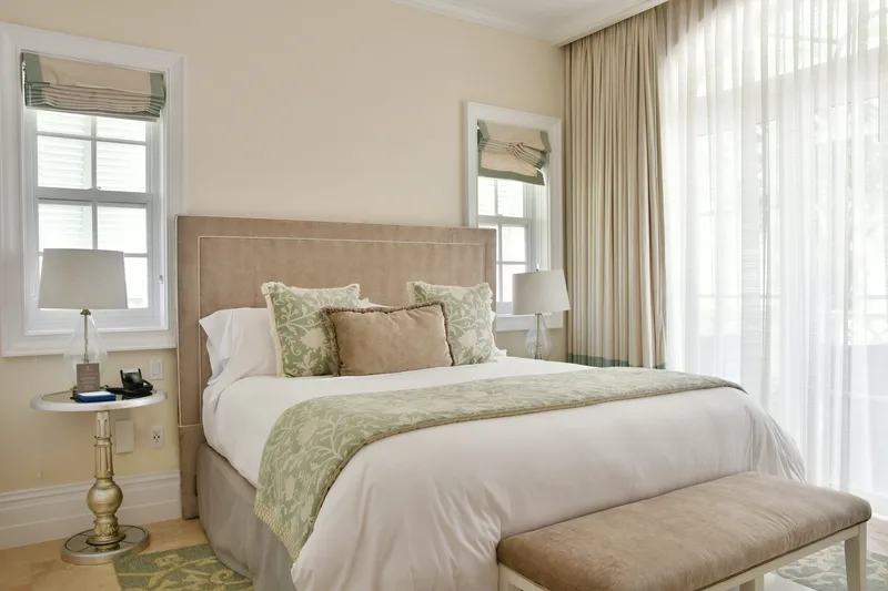 A guest bedroom in beige and sage, with a bench at the foot of the bed