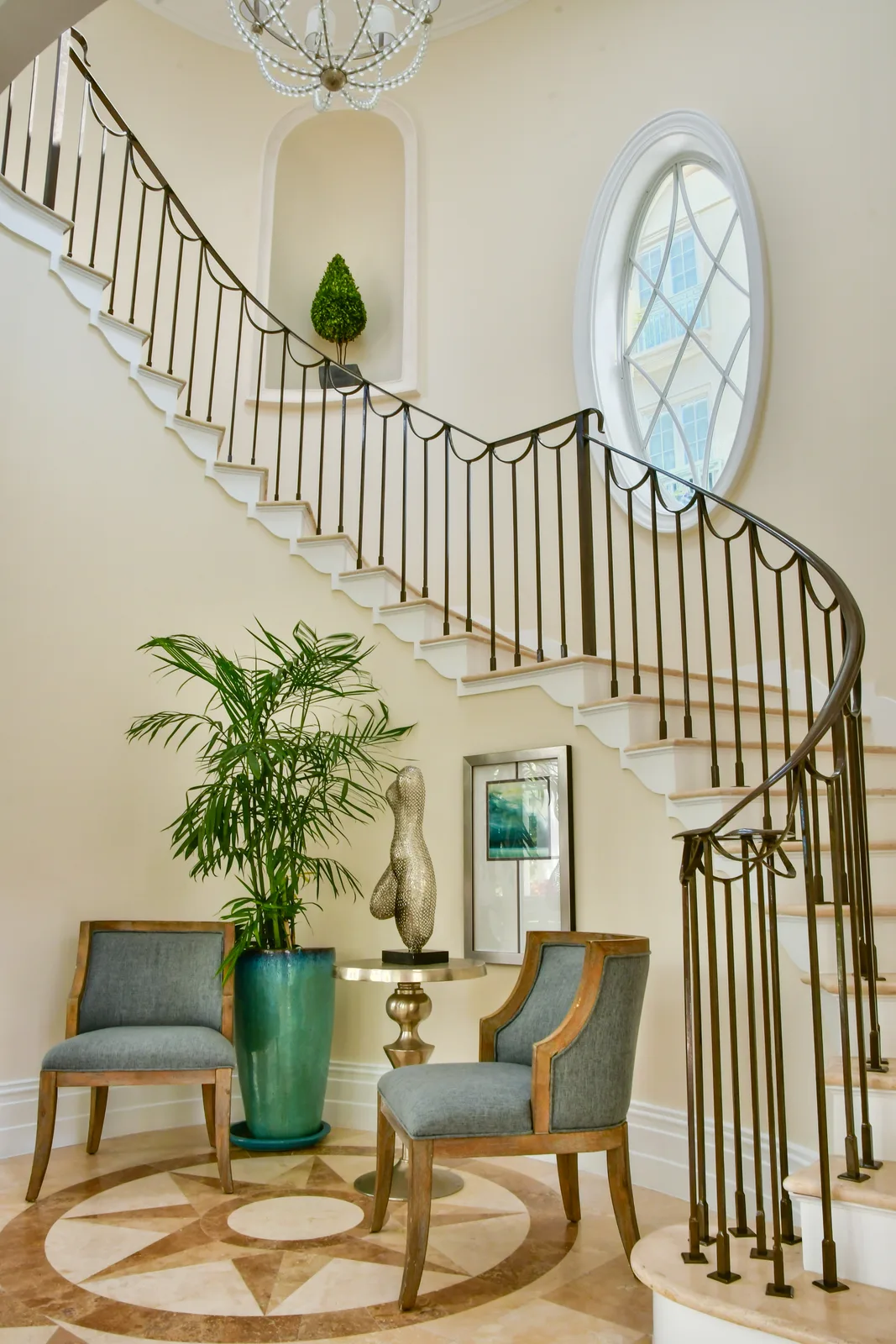 The staircase and its wrought-iron banister under an oval window