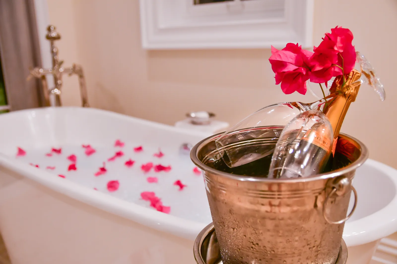 A bath drawn with petals, champagne on ice beside it