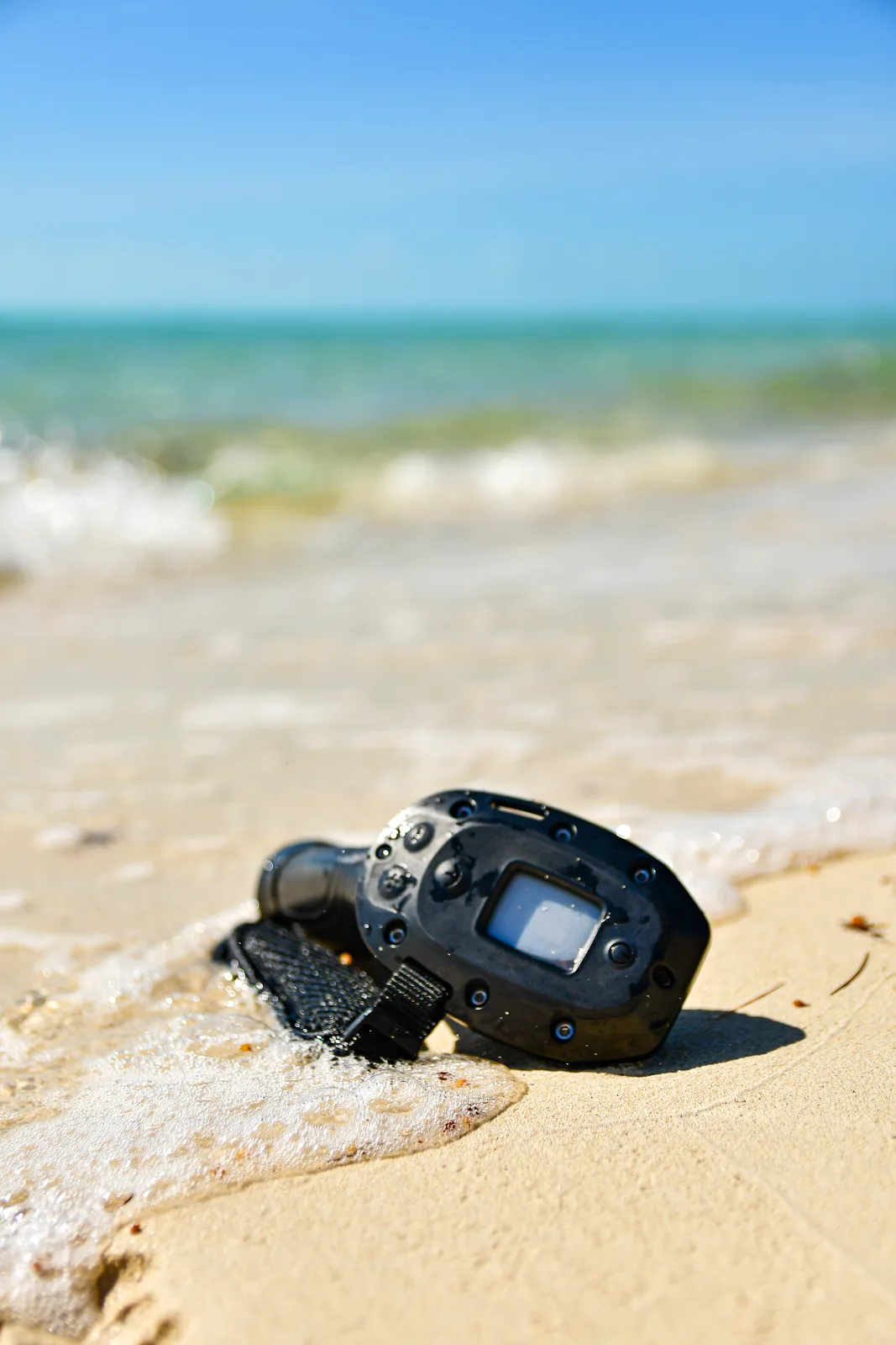 An action camera on the sand, waves behind